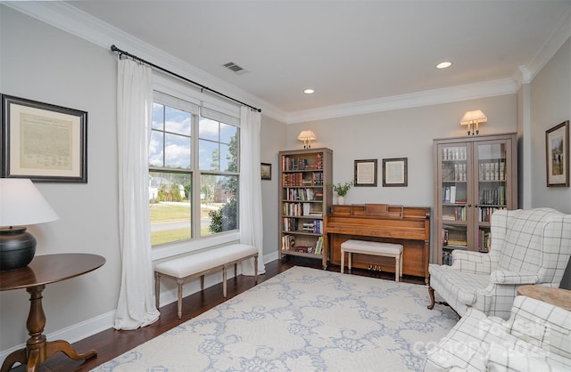 sitting room featuring baseboards, visible vents, wood finished floors, and ornamental molding