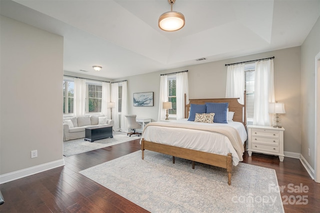 bedroom featuring wood finished floors, a raised ceiling, visible vents, and baseboards