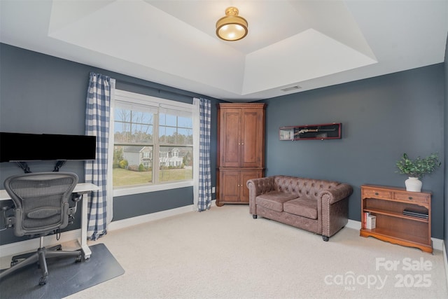 office space featuring a tray ceiling, light colored carpet, visible vents, and baseboards