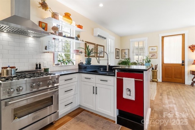 kitchen featuring an AC wall unit, island range hood, stainless steel stove, sink, and white cabinets