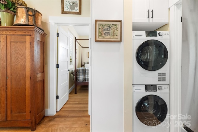 laundry room featuring stacked washer and dryer, light hardwood / wood-style flooring, and cabinets