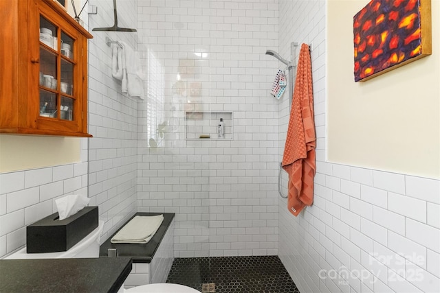 bathroom with a tile shower, tile walls, and toilet