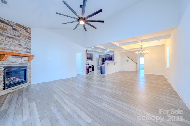 unfurnished living room featuring beam ceiling, coffered ceiling, a fireplace, ceiling fan with notable chandelier, and light wood-type flooring