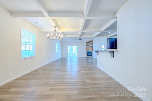 unfurnished living room with coffered ceiling, light wood-type flooring, beamed ceiling, a fireplace, and ceiling fan with notable chandelier