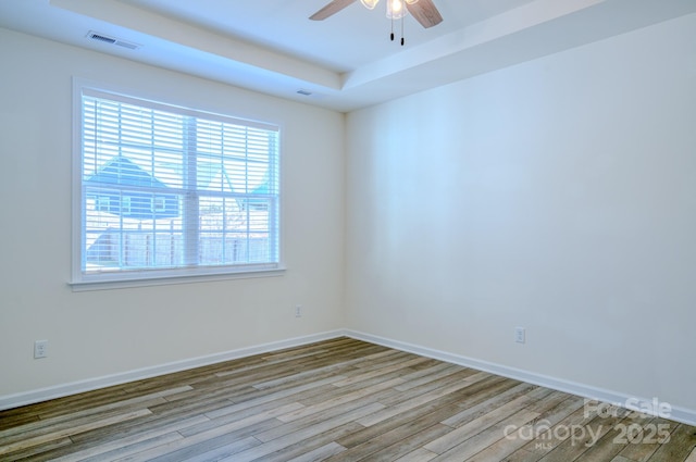 unfurnished room with a tray ceiling, light hardwood / wood-style floors, and ceiling fan