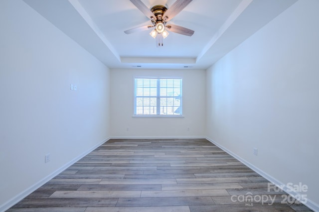 unfurnished room with a raised ceiling, ceiling fan, and light hardwood / wood-style floors