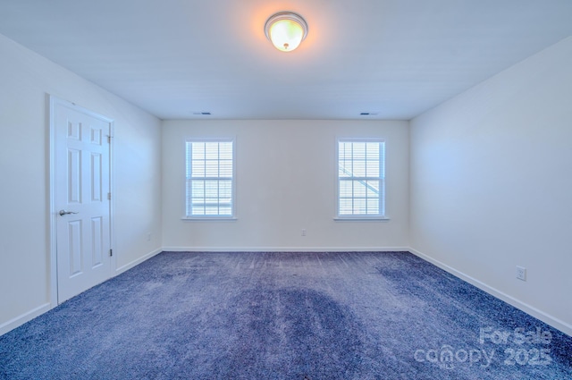 spare room featuring dark colored carpet and a wealth of natural light