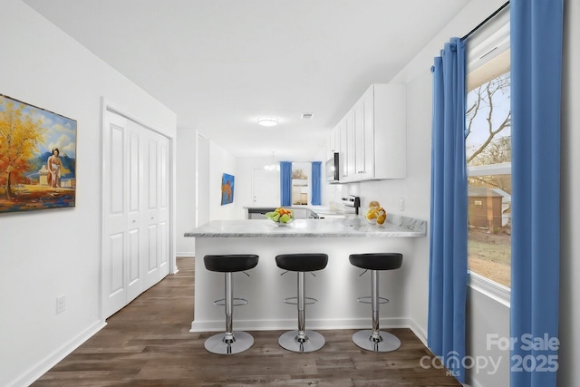 kitchen with white cabinetry, a kitchen bar, kitchen peninsula, and dark wood-type flooring