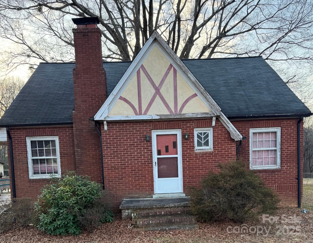 view of front facade featuring entry steps, brick siding, a shingled roof, stucco siding, and a chimney