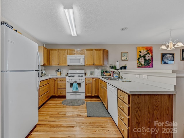 kitchen featuring decorative light fixtures, sink, white appliances, kitchen peninsula, and light wood-type flooring