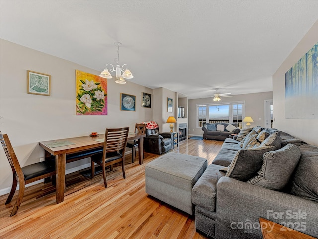 living room featuring ceiling fan with notable chandelier and light hardwood / wood-style flooring