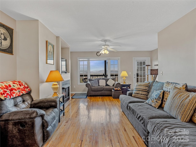 living room featuring ceiling fan, light hardwood / wood-style flooring, and a textured ceiling