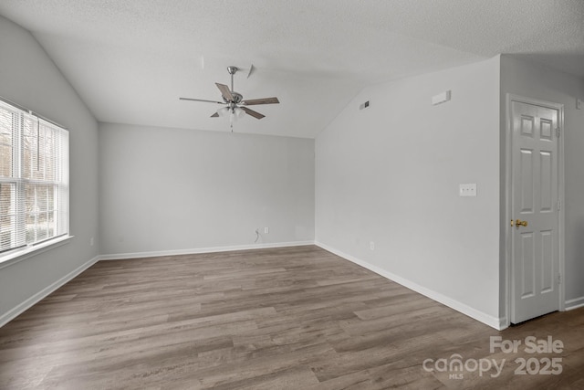 empty room with lofted ceiling, ceiling fan, wood-type flooring, and a textured ceiling