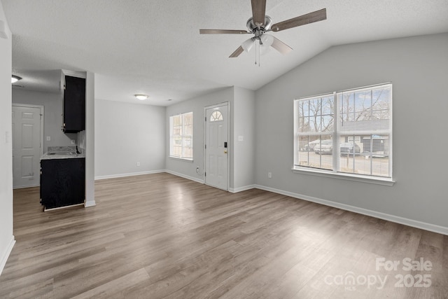 unfurnished living room with vaulted ceiling, light hardwood / wood-style floors, and a textured ceiling