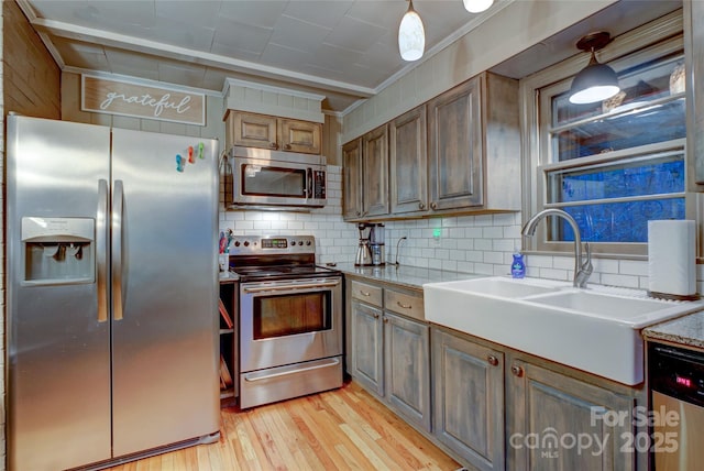 kitchen with sink, tasteful backsplash, light wood-type flooring, appliances with stainless steel finishes, and pendant lighting