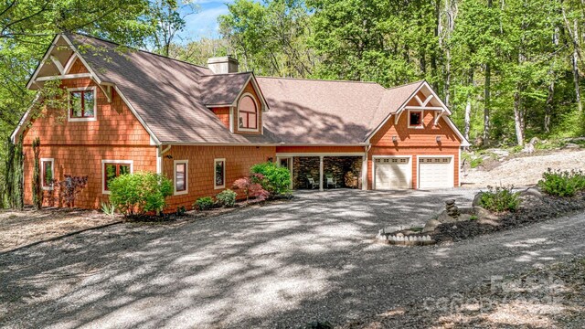 chalet / cabin with a shingled roof, driveway, and a chimney