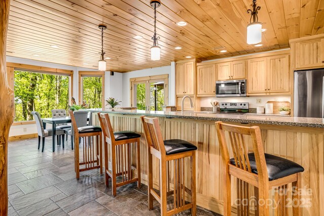 kitchen featuring wood ceiling, light brown cabinetry, appliances with stainless steel finishes, a breakfast bar, and recessed lighting