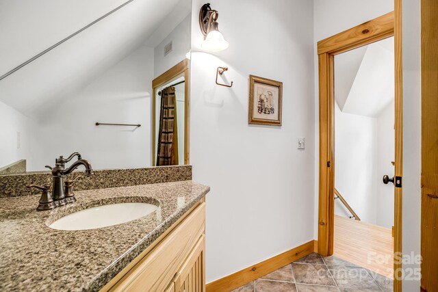 bathroom featuring visible vents, vanity, baseboards, tile patterned floors, and lofted ceiling