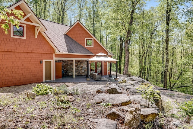 rear view of house featuring a shingled roof, a gazebo, a patio area, and stone siding