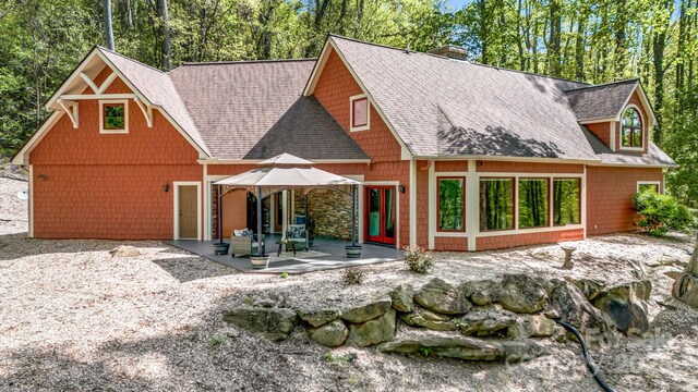 back of house with a patio, roof with shingles, and a chimney