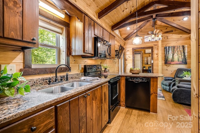 kitchen with wood walls, a peninsula, a sink, light wood-style flooring, and black appliances