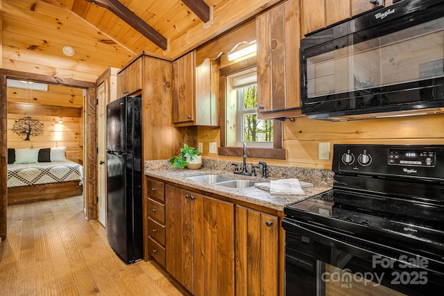 kitchen featuring brown cabinetry, a sink, black appliances, and wood walls