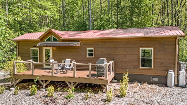 rear view of house featuring a forest view, crawl space, metal roof, outdoor dining area, and a wooden deck