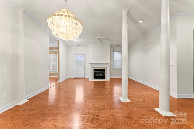 unfurnished living room with ornate columns, crown molding, hardwood / wood-style flooring, and ceiling fan with notable chandelier