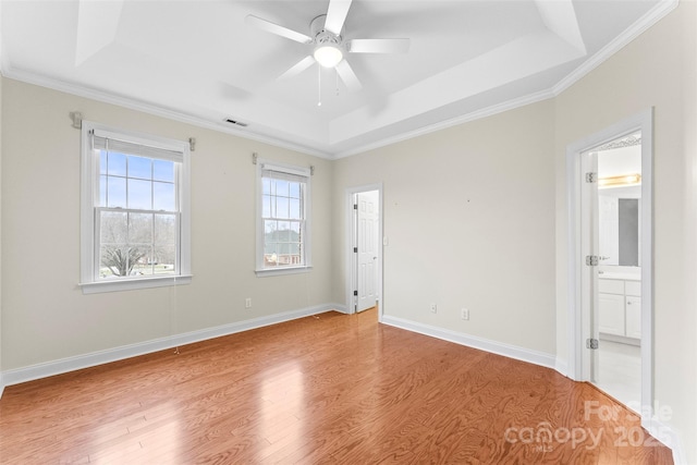 unfurnished bedroom with ceiling fan, ensuite bathroom, a tray ceiling, ornamental molding, and light wood-type flooring