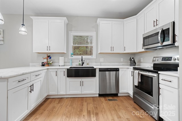 kitchen with sink, white cabinetry, light hardwood / wood-style flooring, pendant lighting, and stainless steel appliances