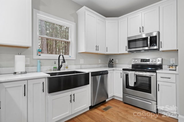 kitchen featuring sink, light hardwood / wood-style flooring, appliances with stainless steel finishes, white cabinetry, and light stone countertops