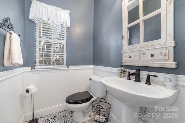 half bath featuring a wainscoted wall, toilet, and tile patterned flooring