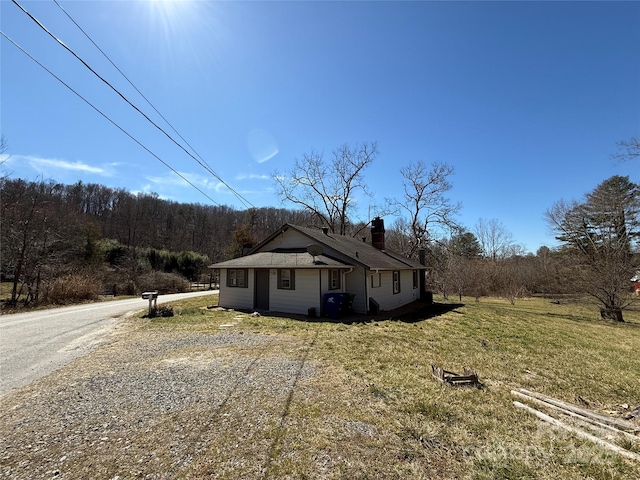 view of front of property with gravel driveway, a chimney, and a front lawn