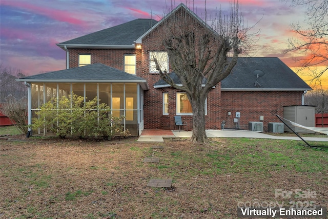 back house at dusk with central AC unit, a lawn, a sunroom, and a patio