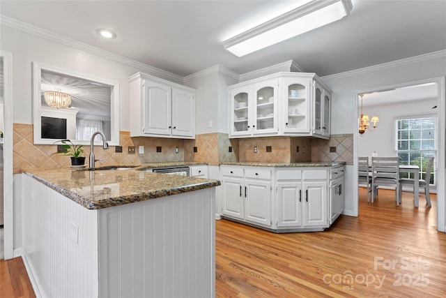 kitchen with sink, a chandelier, kitchen peninsula, light hardwood / wood-style floors, and white cabinets