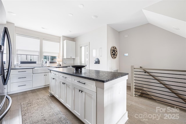 kitchen with white cabinetry, black refrigerator, a center island, and light wood-type flooring