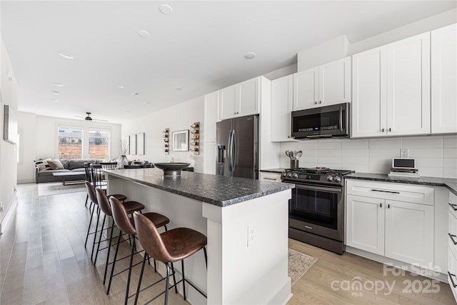 kitchen featuring stainless steel appliances, a kitchen breakfast bar, a center island, tasteful backsplash, and white cabinets