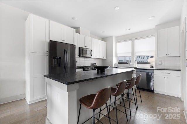 kitchen with a kitchen island, hardwood / wood-style floors, white cabinetry, a breakfast bar area, and stainless steel appliances