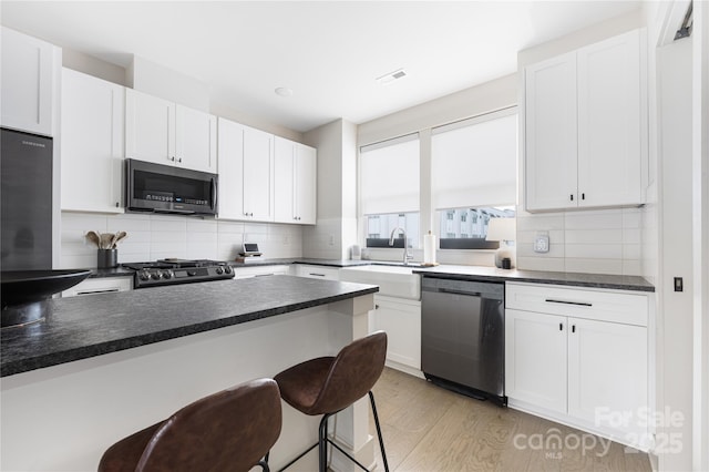 kitchen featuring white cabinetry, dishwasher, sink, a kitchen breakfast bar, and stove