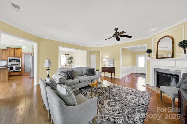 living area with visible vents, a high end fireplace, ceiling fan, ornamental molding, and hardwood / wood-style floors