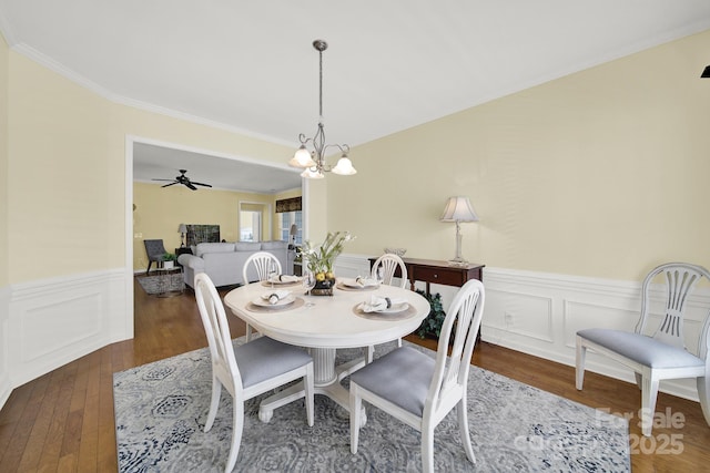 dining area featuring ceiling fan with notable chandelier, ornamental molding, wainscoting, and hardwood / wood-style flooring