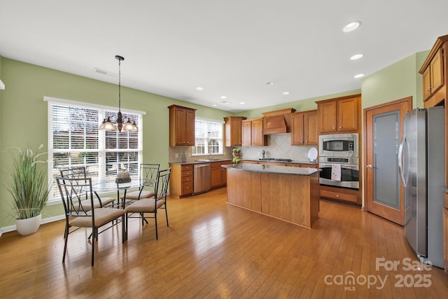 kitchen featuring a center island, light wood-type flooring, stainless steel appliances, wall chimney range hood, and decorative backsplash