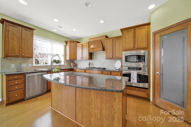 kitchen featuring a sink, appliances with stainless steel finishes, a center island, custom exhaust hood, and visible vents