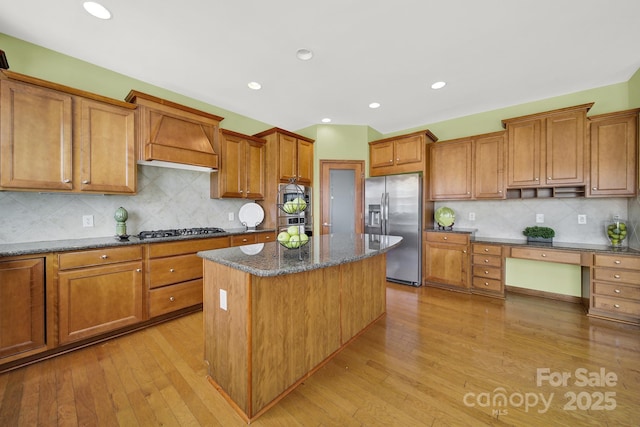 kitchen with light wood finished floors, premium range hood, a center island, gas cooktop, and stainless steel refrigerator with ice dispenser