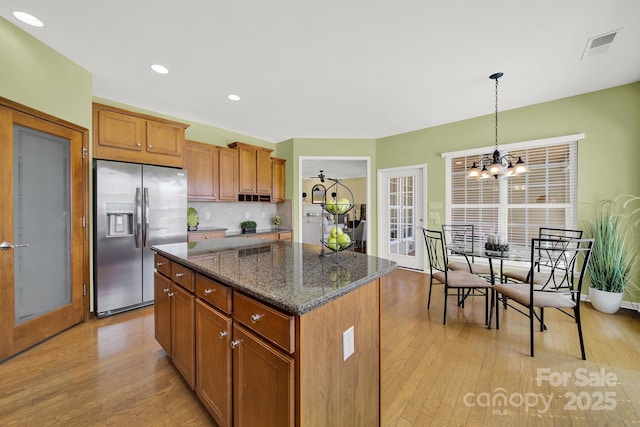 kitchen with light wood finished floors, stainless steel fridge with ice dispenser, brown cabinetry, and a kitchen island