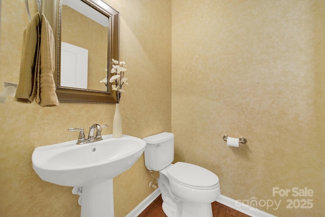 half bathroom with baseboards, toilet, a sink, and wood finished floors