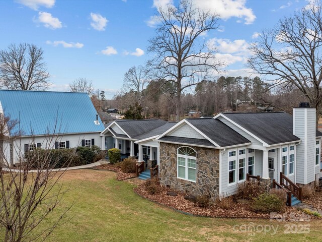 rear view of property with a lawn, stone siding, roof with shingles, and a chimney