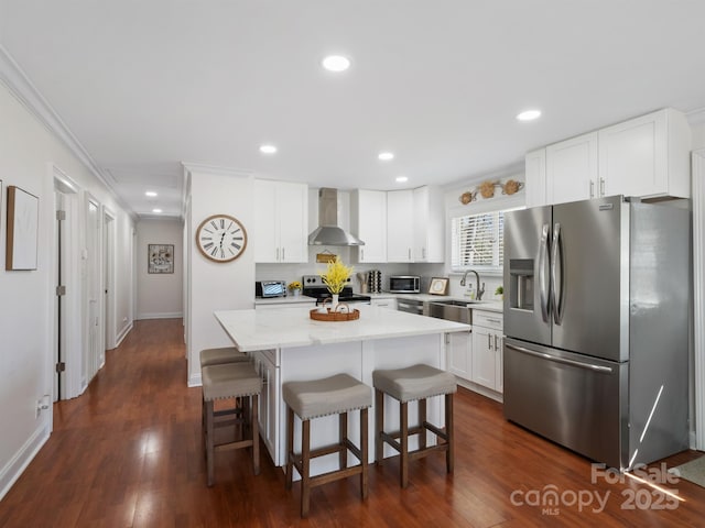 kitchen with a kitchen island, appliances with stainless steel finishes, a kitchen breakfast bar, wall chimney range hood, and a sink