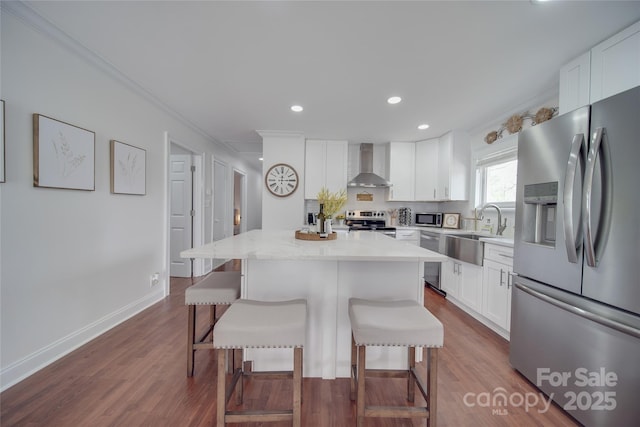 kitchen featuring a breakfast bar area, stainless steel appliances, a sink, wall chimney range hood, and a center island