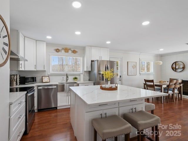 kitchen with appliances with stainless steel finishes, dark wood-type flooring, a breakfast bar area, and white cabinetry